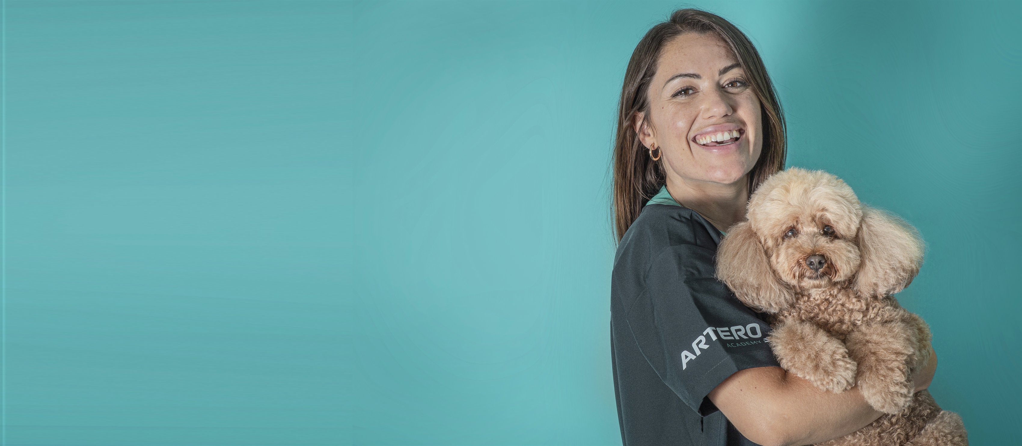 Una alumna sonriente de Artero Academy abraza a un caniche toy sobre un fondo turquesa
